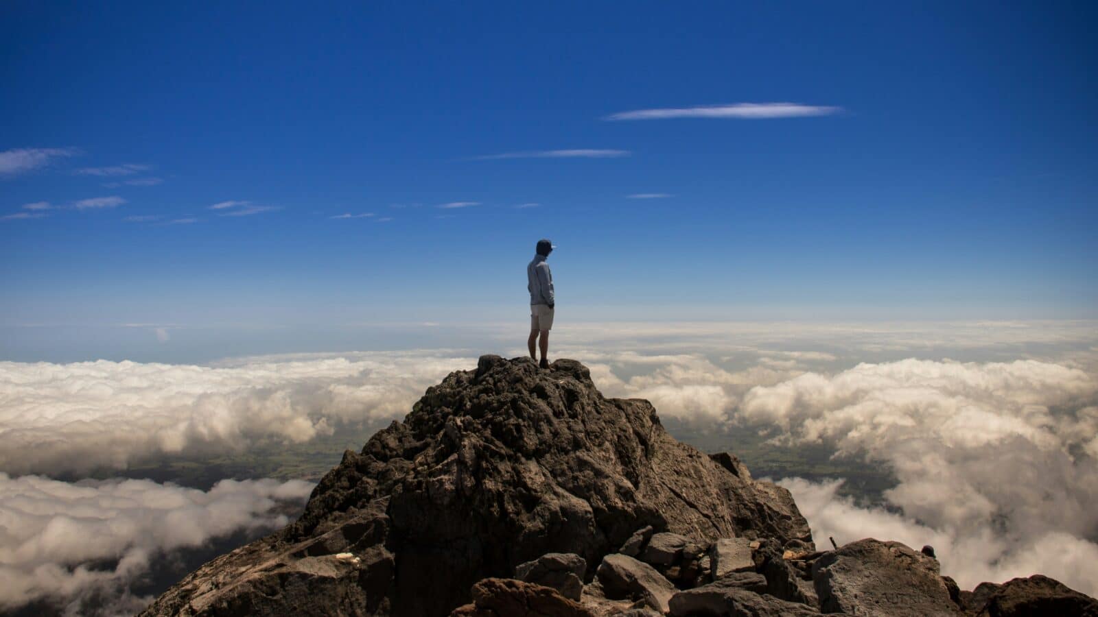 Person auf einem Berggipfel über den Wolken – Symbol für Leadership, Klarheit, Weitblick und bewusste Führung.